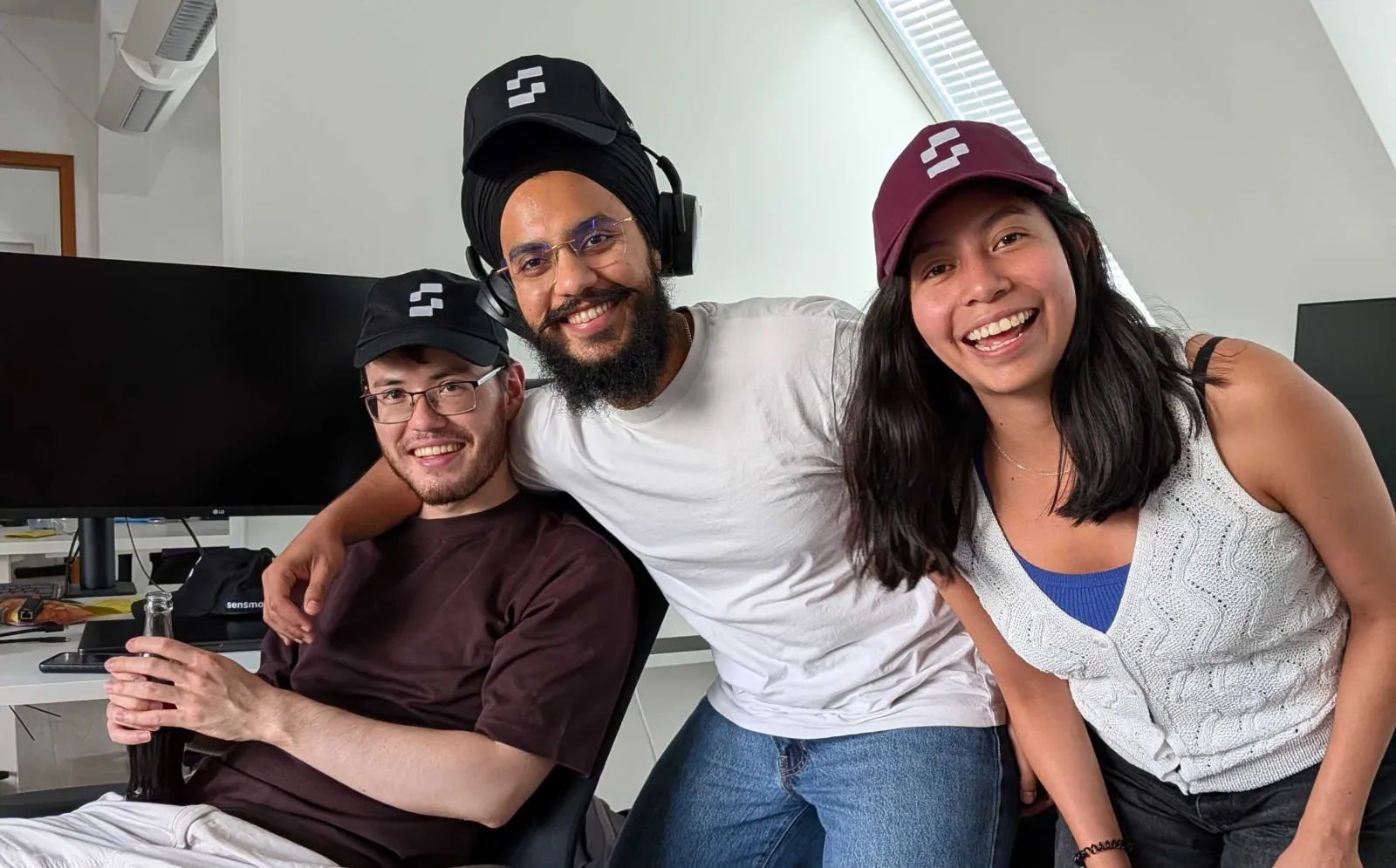 Three sensmore team members in sensmore caps, smiling together in the office